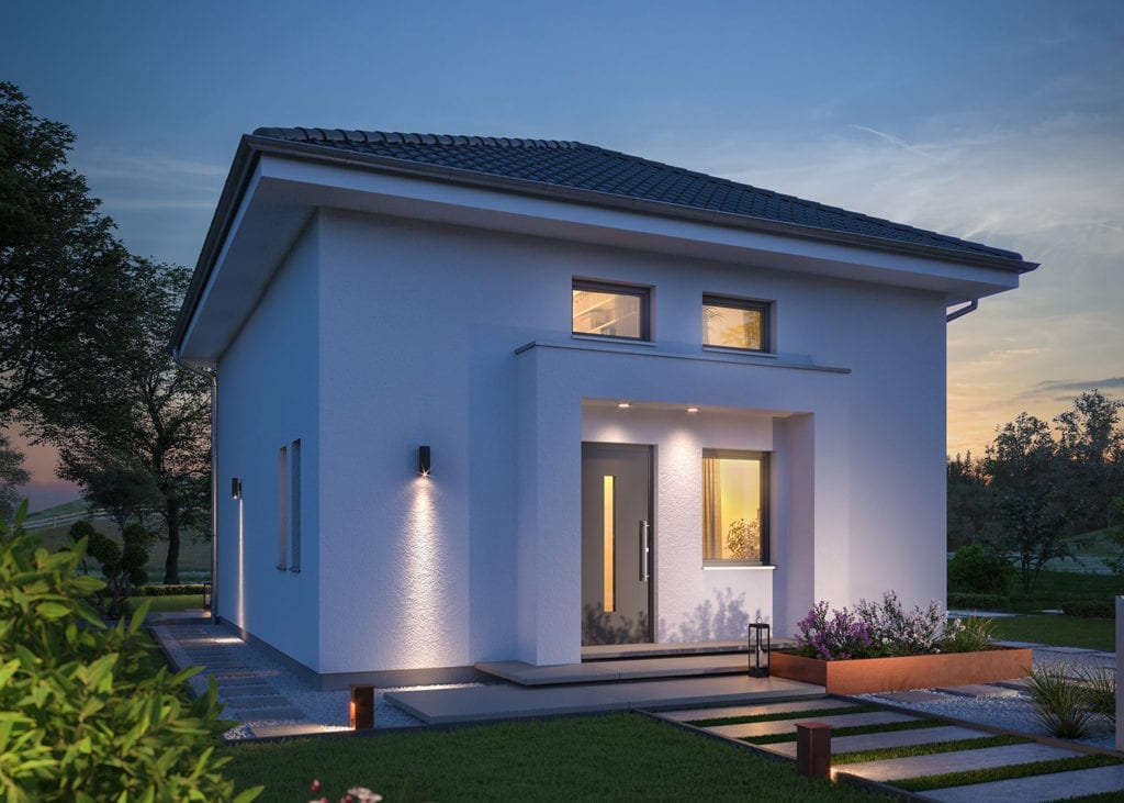 Stimmungsvolle Rückansicht einer modernen massa haus Fertighaus-Stadtvilla bei Dämmerung, die durch warme Außenbeleuchtung und hell erleuchtete Innenräume einladend wirkt. Die großzügige Terrasse mit Ess- und Loungebereich bietet viel Raum für einen entspannten Lifestyle.