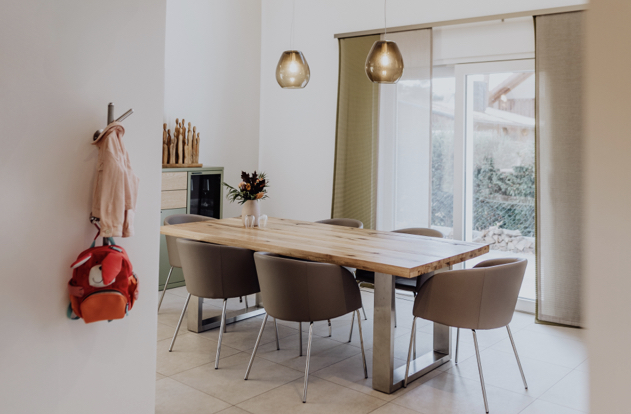 Gemütlicher Essbereich mit massivem Holztisch, stilvollen Sesseln, Hängeleuchten und Blick in den Garten.