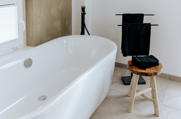 Schlichtes und elegantes Badezimmer mit freistehender Badewanne, schwarzen Akzenten und Holzhocker für Handtücher